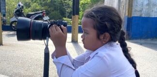 bocah perempuan berseragam sekolah dasar (SD) sedang memotret menggunakan kamera DSLR layaknya seorang fotografer.